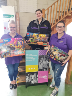 Three female volunteers from The Sixth Child holding donated toys and games from GIVIT.