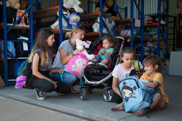 A mum crouching in front of a warehouse to hand out donated items such as toys and bags to her four children, two older girls, and two younger boys