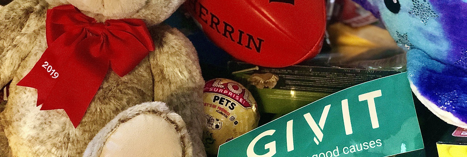 A GIVIT sticker sitting amongst a jumble or presents including teddy bears, soft toys and a red AFL ball.