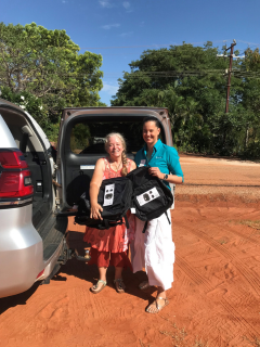 Engagement Officer Lisa handing donated school bags over to a support organisation worker, both standing on red dirt next to a 4wd.