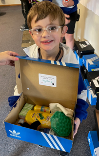 A young boy holding a shoebox of toiletries that's been given to him