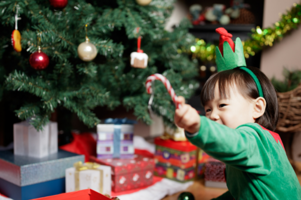 A little girl in a Christmas festive costume waving a candy cane in front of a Christmas tree