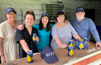 GIVIT staff member Caroline Odgers with volunteers from Bega Devils Soccer Club standing in the canteen and holding Hughies Beer.