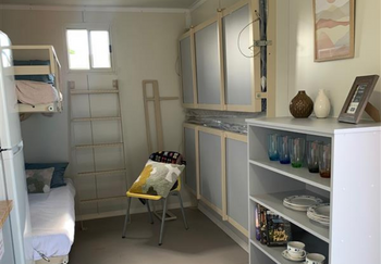 The interior of a temporary housing pod in Wollongbar, NSW. Pictured is a set of bunk beds, shelving and a chair.