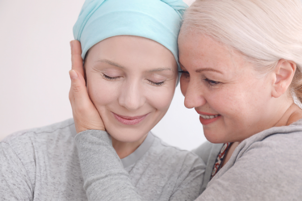 A young woman with a blue bandanna suffering from cancer being embraced by an older woman